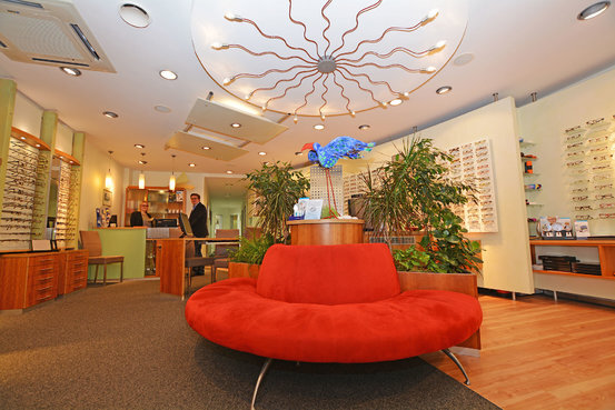 Modernes Optikergeschäft mit rotem Sofa, Brillenauswahl und einladender Atmosphäre.